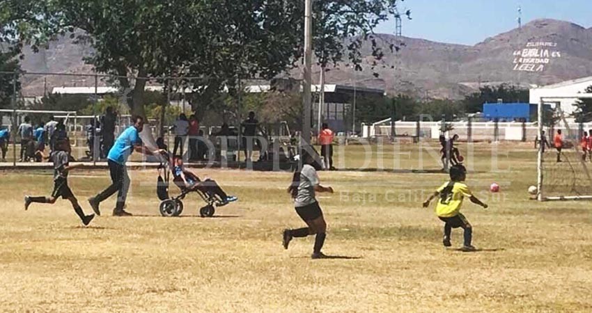 Papá impulsa a su hijo en silla de ruedas para que juegue futbol